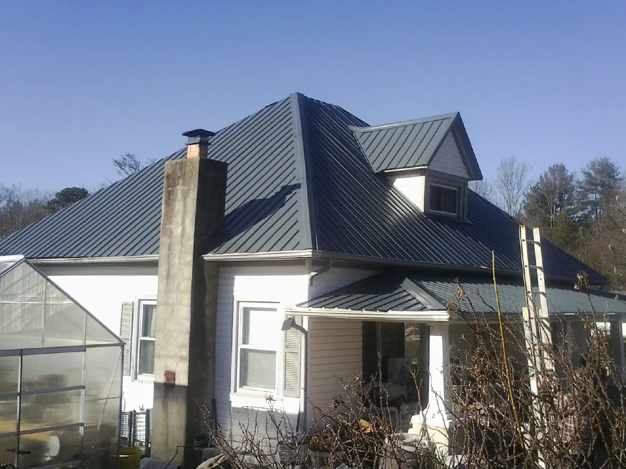 Dark blue standing seam metal roof on a white farmhouse with dormer — Slate & Tile Roof Repair by Roofing Brothers in Menno