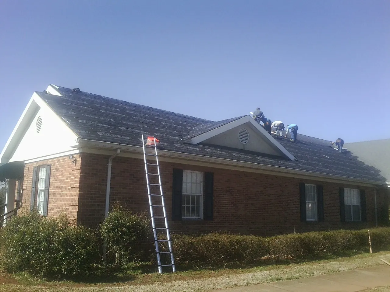 Crew tearing shingles off a brick ranch roof with a ladder set — Metal Roof Repair work by our crew in Menno