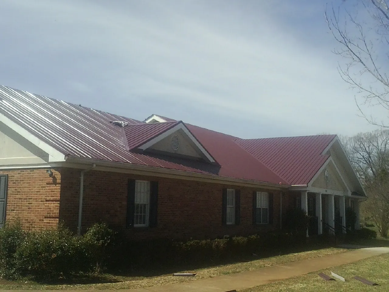 Red metal roof with gabled entries on a long brick building, from a Hail Damage Roof Repair job in Menno