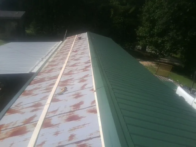 Old rusted panels beside newly installed green metal roofing — Wind Damage Roof Repair by Roofing Brothers in Menno