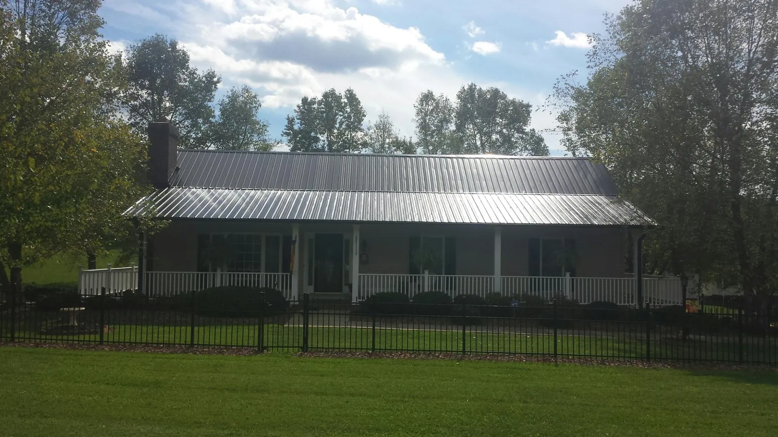Gray metal roof on a brick ranch with a full width front porch — Gutter Guard Installation work by our crew in Menno