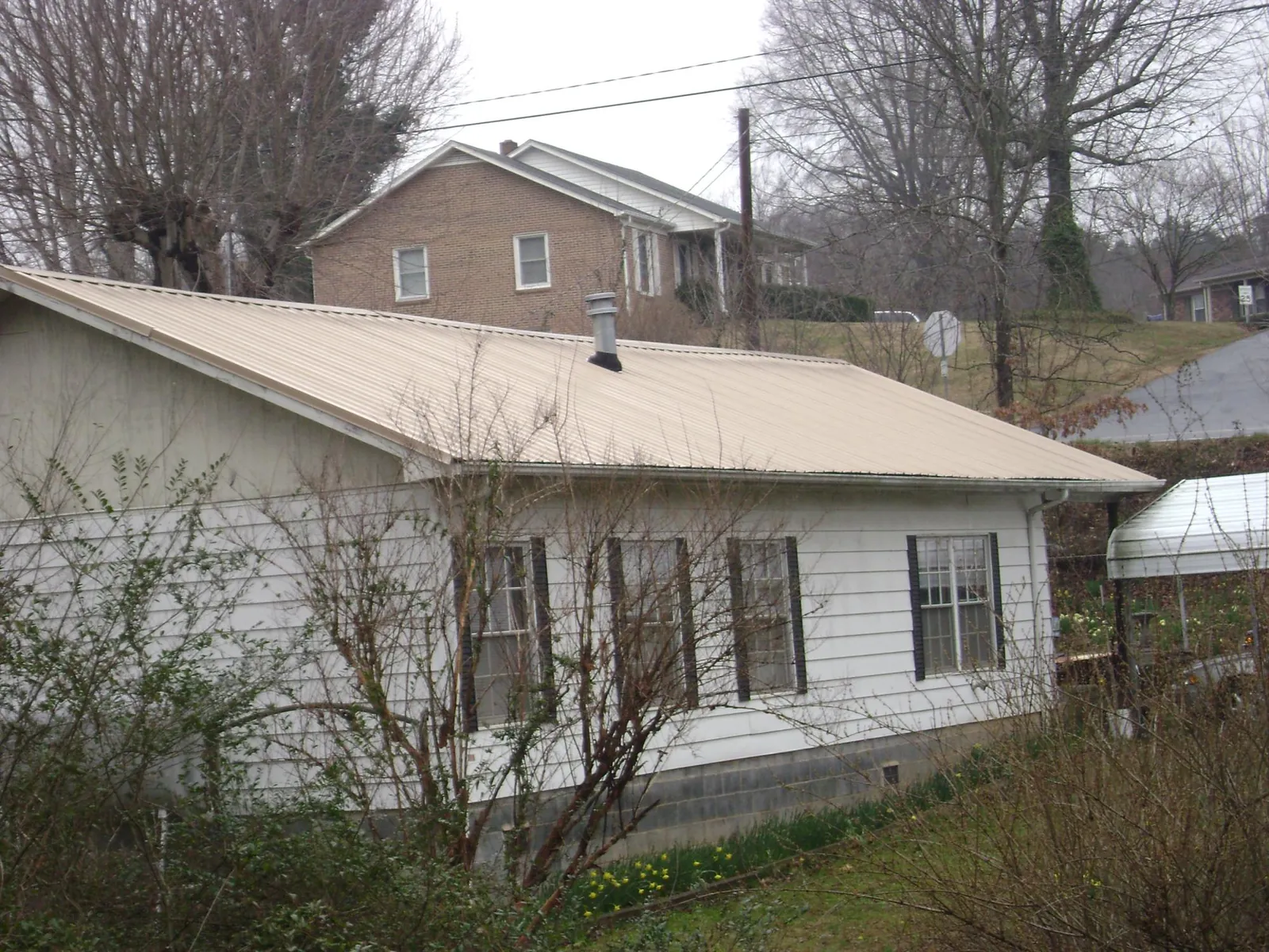 Tan metal roof on a white sided house set into a hillside — Commercial Roofing by Roofing Brothers in Menno